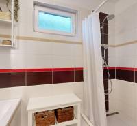 A bathroom in a family house with a window, a shower, and shelves for small items.
