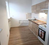 A kitchen in a studio apartment with a kitchenette and a stove, flooring with a wooden decor.