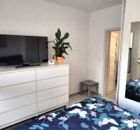 Bedroom in a 2-room apartment with white furniture, a mirror, and a TV on the dresser.