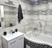 A bathroom in a 2-room apartment with a corner bathtub and gray tiles.