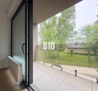 A balcony of a 2-room apartment with a view of greenery and glass railing.