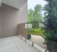 A balcony with glass railings offering a view of greenery in a 2-room apartment.