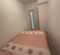 A bedroom in a 2-room apartment with a bed featuring a floral motif and light-colored walls.