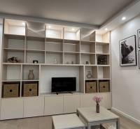 A storage wall with shelves and decorations in a 2-room apartment, next to a table with flowers.