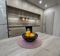 A kitchen with light cabinets and a bowl of fruit on a wooden table in a 2-room apartment.