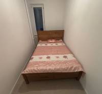 A narrow bedroom in a two-room apartment with a wooden bed and a floral bedspread.