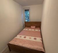 A narrow bedroom with a bed with a patterned pink blanket in a two-room apartment.