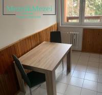 Dining area in a 2-room apartment with wooden decor on the walls and tiles.