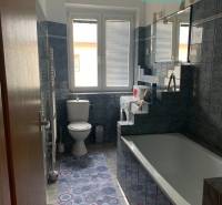 Bathroom in a 2-room apartment with a bathtub, washing machine, and dark tiles.