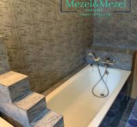 A bathroom with steps and a bathtub surrounded by gray tiles in a two-room apartment.