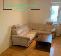 Living room in a two-room apartment with a corner sofa and a table on a floor with a wooden decor.