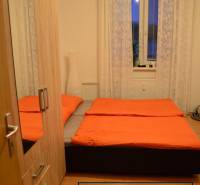 Bedroom in a two-room apartment with orange blankets, wardrobe, and lamp, floor with wooden decor.
