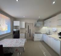 A kitchen in a 3-room apartment with white cabinets and tiles, and a floor with a wooden design.