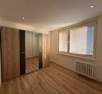 A bedroom in a three-room apartment with a wooden decor floor and a built-in wardrobe.