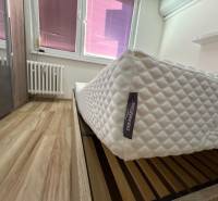 A bedroom with wood-patterned flooring, a quality mattress, and a large radiator in a 3-room apartment.