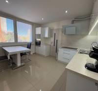 The kitchen of a 3-room apartment with large windows, a dining table, and light flooring.