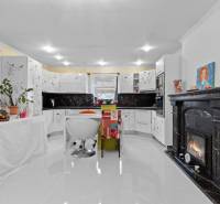 A kitchen in a family house with a fireplace, white cabinets, and plants, with a wooden decor floor.