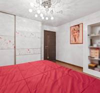 A bedroom in a family house with a red bed, a wooden decor floor, and a wardrobe.