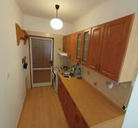 A kitchen with a wood-patterned floor, a kitchen unit, and a gas stove in a two-room apartment.