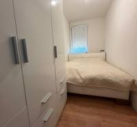 A bedroom in a two-room apartment with a white bed, wardrobe, and wooden decor flooring.