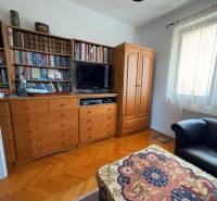 A room in a multi-room apartment with a library, a television, and a floor with a wooden decor.