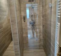 Shower corner with ceramic tiles and a wooden decor floor in a cottage.