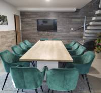 A dining room in a cabin with wooden decor, a staircase, and green chairs around the table.