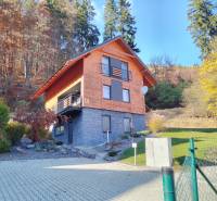 A cottage in Stráne in Martin surrounded by an autumn forest and a manicured lawn.