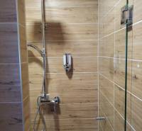 Shower corner in a cabin with wood-patterned tiles, large rain shower.
