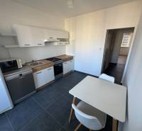 A kitchen in a 3-room apartment with white cabinets and a table on a dark floor.
