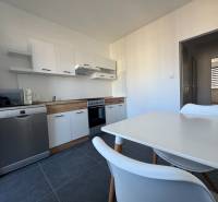 The kitchen of a three-room apartment with white furniture and appliances, ceramic tile flooring.
