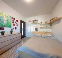 Bedroom in a family house with a bed, shelves, paintings, and a wooden decor floor.