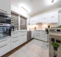 A kitchen in a family house with white cabinets and a window with blinds.