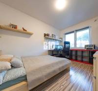 A bedroom in a family house with a desk, shelves, and a wooden decor floor.
