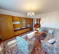 Living room in a family house with a wooden wall unit and a patterned sofa set.