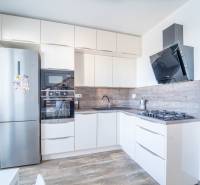 A kitchen in a 3-room apartment with white furniture, built-in appliances, and a wooden decor floor.