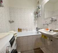 Bathroom in a 3-room apartment with a washing machine, sink, and bathtub, tiled with light tiles.