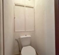 A toilet in a 3-room apartment with a simple design and white walls.