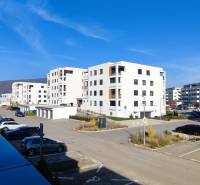 A set of white apartment buildings on Predmerského Street in Trenčín with parking spaces.