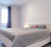A bedroom in a two-room apartment with light furniture and a wooden decor floor.