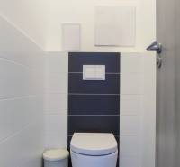 A toilet with white tiles and a wall-hung toilet bowl in a 2-room apartment.