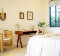 A bright bedroom in a family house with a rattan chair and a wooden table.