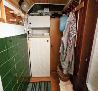 The cottage has a narrow entrance with coat curtains, a shelf, and green paneling.