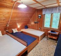 Interior of a cabin with wooden walls, three beds, a window, and a floor with a wooden decor.