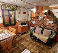 The interior of a cabin with a sofa, wooden decor flooring, a dining table, and a staircase.