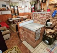 The interior of a cottage with a traditional brick stove, a wooden-patterned floor, and comfortable seating.