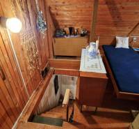Wooden walls in a cabin with a bed, stairs, and decorative items on the table.