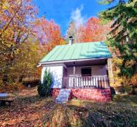 The cottage at Tály in Bystrá surrounded by colorful autumn nature with a bench in the foreground.
