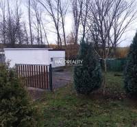 Recreational plots in Nitrianske Rudno, trees, bushes, and fencing near the white building.