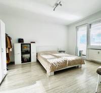 A bedroom in a studio apartment with a wood-patterned floor and light-colored furniture.